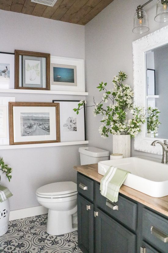 an airy bathroom with a grey vanity and a butcherblock countertop, white appliances, ledges with pics and fresh white blooms