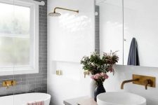 an airy contemporary bathroom with a grey subway tile accent wall, blue and white tiles on the floor, a floating vanity, brass fixtures and a window