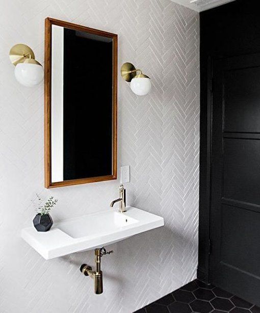 an elegant vintage-inspired bathroom with white and black tiles, a floating sink, greenery in a vase and brass sconces on the wall