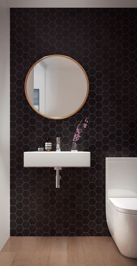an ultra-modern powder room with black hexagon tiles, a floating sink, a white toilet and a round mirror - nothing else is needed