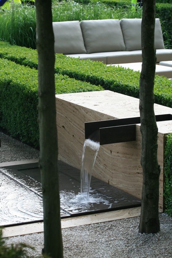 a modern and super simple waterfall with a stone slab, a large metal faucet and a metal bowl underneath to catch the water