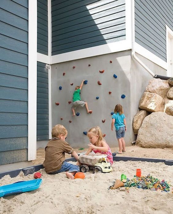 an outdoor kids' playspace with a climbing wall, rocks and a sandbox is a great space for lots of children