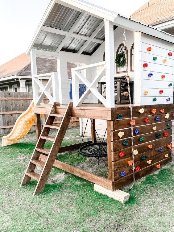 a color block kids' playhouse outdoors, with a stained chair, a ladder, some decor and a colorful climbing wall