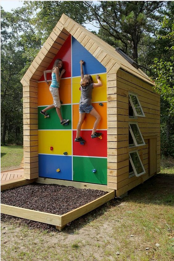 a colorful garden house for kids, with windows and a small yet cool climbing wall that hides storage space at the same time