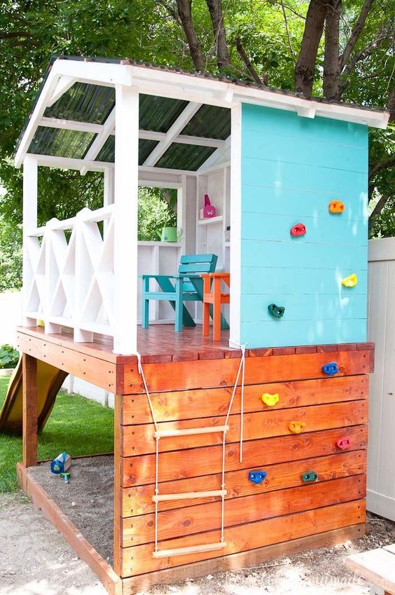 a colorful outdoor kids' playhouse with a climbing wall, a rope ladder and colorful wooden furniture plus a slide