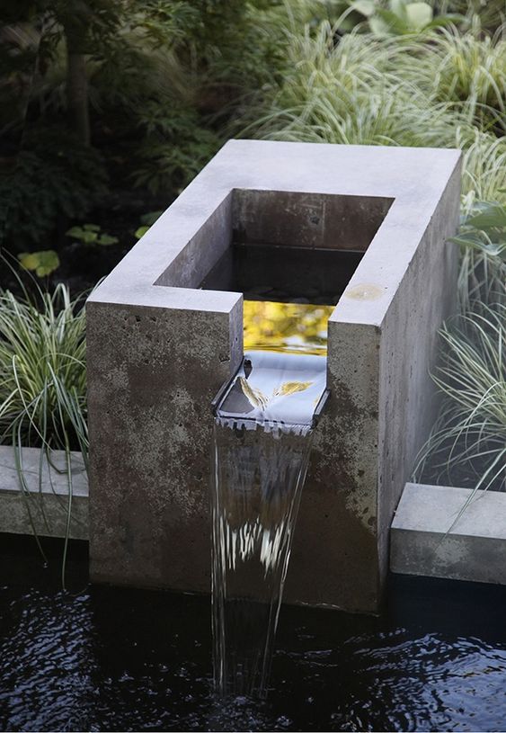 a modern waterfall of concrete flowing into a bowl of concrete and surrounded with grasses is a lovely idea for a minimalist space