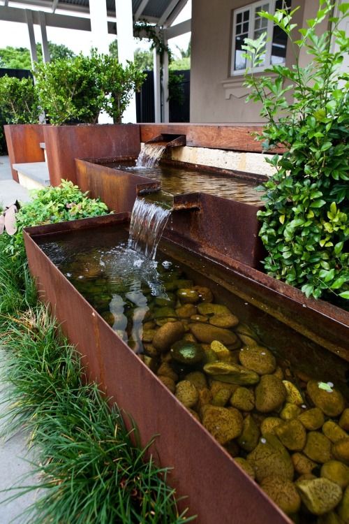 a modern waterfall with several faucets and bowls, with rocks inside and greenery around is a cool idea for a modern garden