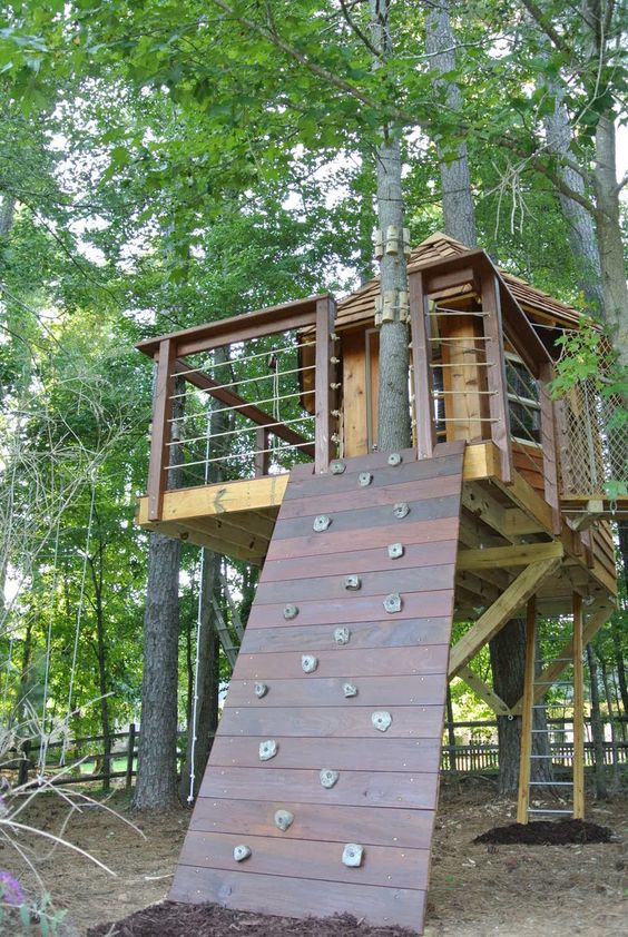 a gorgeous stained wood tree house with living trees, a climbing wall and a ladder is a lovely idea for a rustic outdoor space a gorgeous stained wood tree house with living trees, a climbing wall and a ladder is a lovely idea for a rustic outdoor space