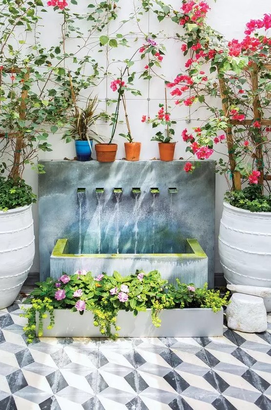 a beautiful modern waterfall of a wall with multiple faucets, a concrete tub and a matching planter with blooms next to it