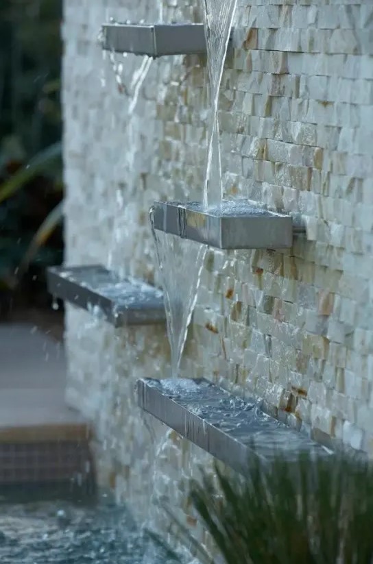 a creative modern waterfall of a faux stone wall and metal shelves is a lovely idea for a modern garden