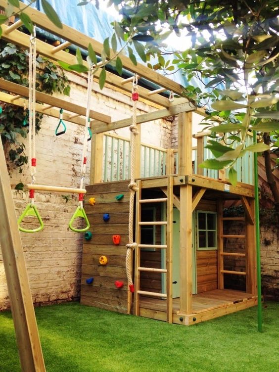 a kids' playground with a wooden house with ladders and a platform on top, with a climbing wall, some rope for climbing and other stuff