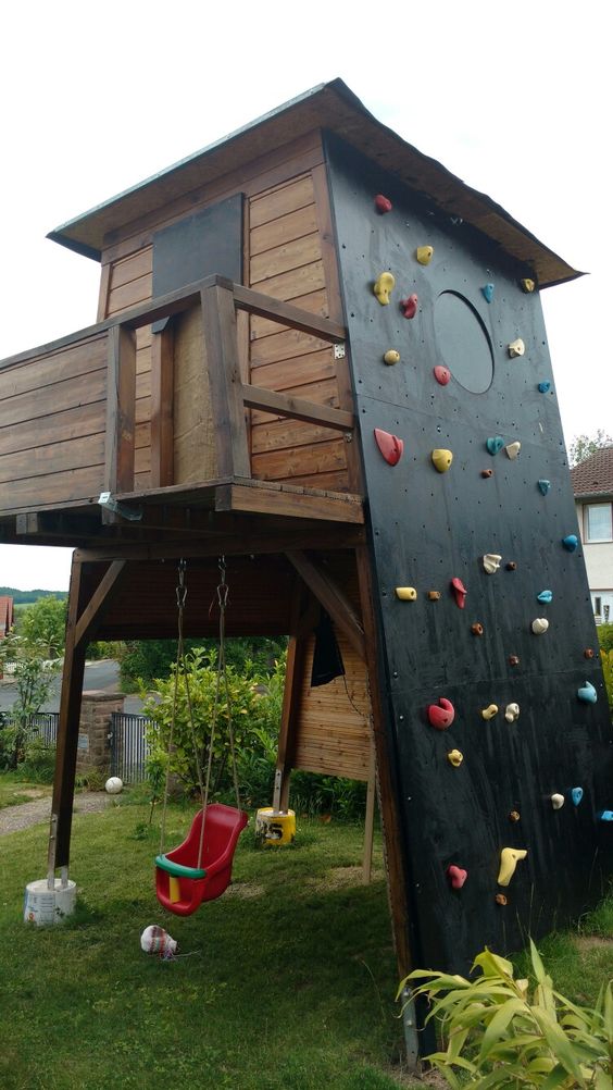 a kids' playhouse with a swing, a room on top and a black climbing and a round window is a lovely idea for a garden a kids' playhouse with a swing, a room on top and a black climbing and a round window is a lovely idea for a garden