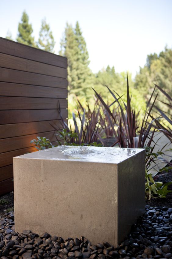 a minimalist stone slab fountain surrounded with black pebbles is a bold and cool solution for a contemporary space