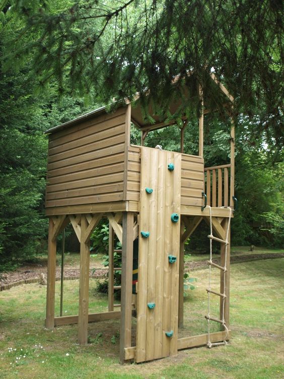 a light-stained wooden house with a rope ladder, a small climbing wall under the trees is a lovely idea for kids to have fun