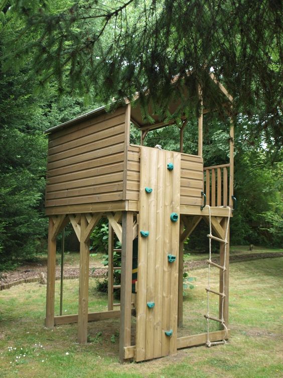 a light stained wooden house with a rope ladder, a small climbing wall under the trees is a lovely idea for kids to have fun a light-stained wooden house with a rope ladder, a small climbing wall under the trees is a lovely idea for kids to have fun