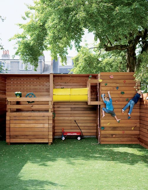 a light-stained wooden playground with a climbing wall, a ship imitation and a tube for kids to play