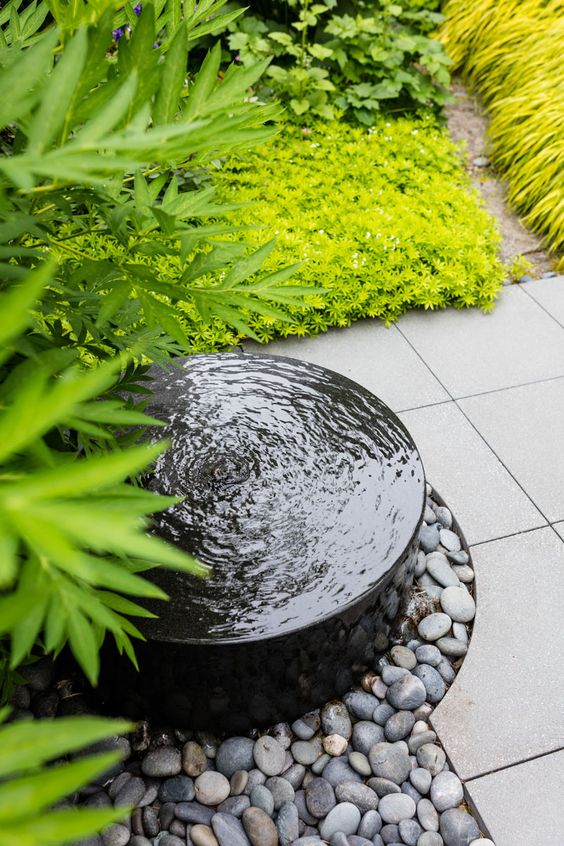 a modern bowl fountain surrounded with pebbles and super bold grasses and grasses is a lovely idea for a modern garden
