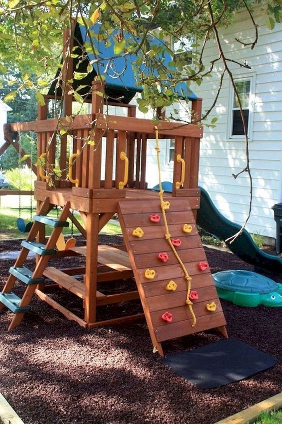 a small stained playhouse with a green slide, a ladder, a climbing wall, a dining set under the house is a fun and cool idea to rock