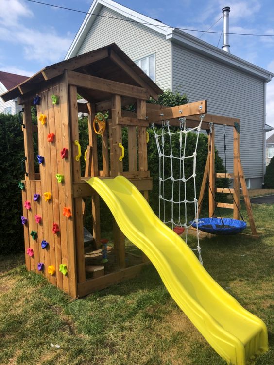 a small stained wood playing complex with a creative swing, a rope ladder, a climbing wall and a slide is a lovely space