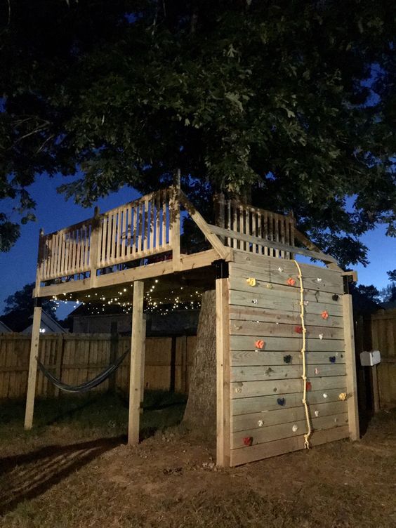 a treehouse platform built around a living tree, featuring a climbing wall and rope is a lovely idea for outdoors