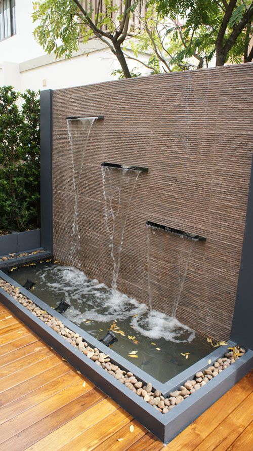 a modern wall fountain of stone and metal, with spotlights to light it up at night, pebbles around it