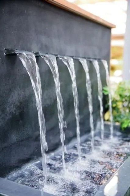 a stylish modern fountain coming out of the wall and falling into a bowl with pebbles is a lovely idea for a modern or minimalist space