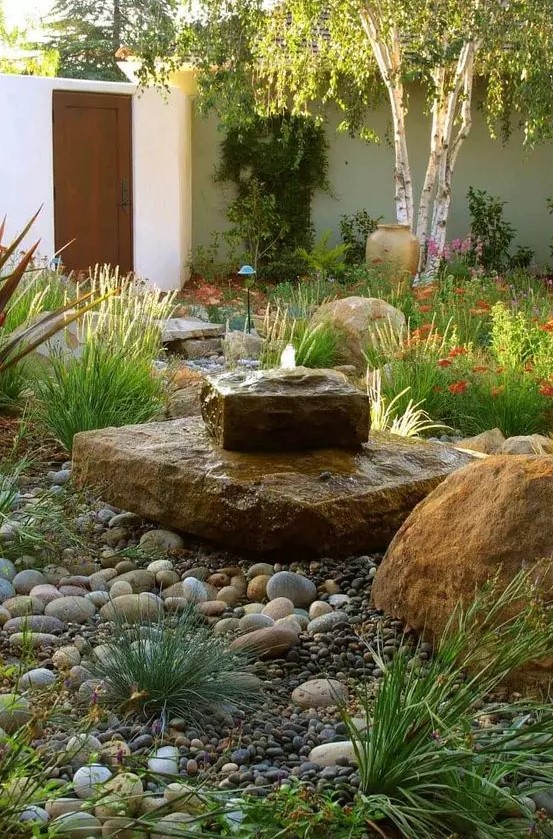 a unique and bold stone slab fountain, landscaping and pebbles around create a gorgeous look in the garden