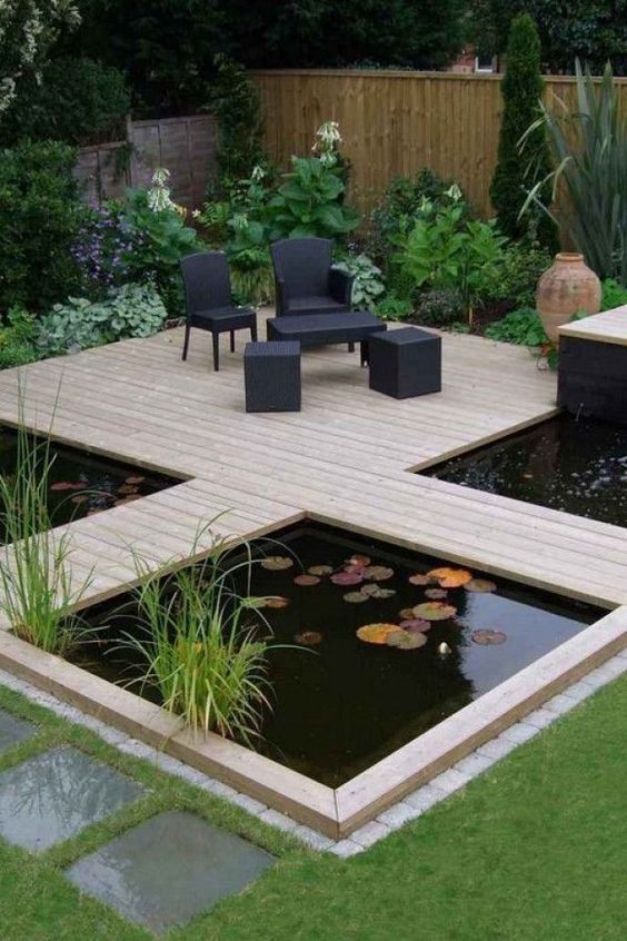 a modern garden with green lawn and some blooms, a wooden deck with black outdoor furniture, a couple of ponds