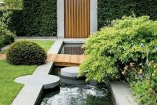 29 a modern garden with lots of greenery and bushes, with a water feature, stone pavements and a pathway over the water feature