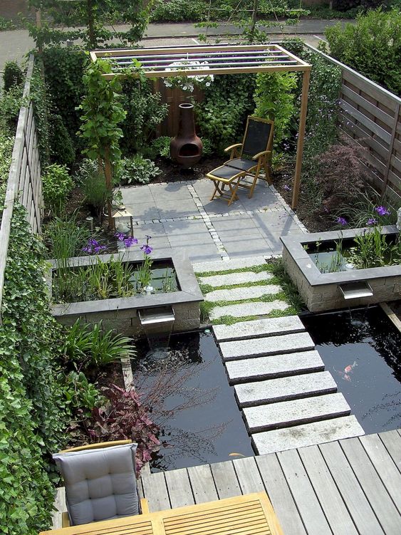 a modern outdoor space with a deck, a dining set, a pond with stone steps, a stone deck with some furniture and water gardens