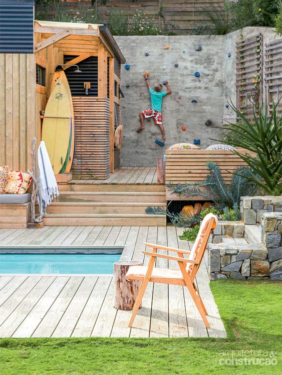 a modern outdoor space with a small pool, a wooden deck, built-in and usual furniture of wood, a small outdoor shower and a climbing wall for kids