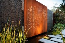 38 an ultra-modern outdoor space with a jaw-dropping orange accent wall with art, a large lit up water feature with stone pavements and water plants