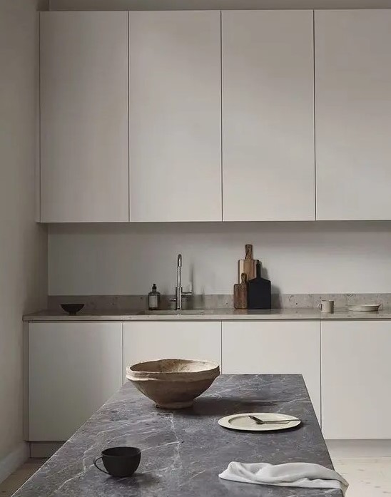 a Nordic greige kitchen with sleek cabinets, a neutral stone countertop, a grey stone table and pretty tableware