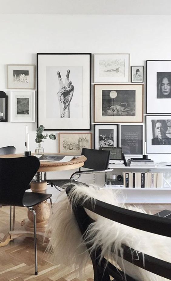 a Nordic home office with a round stained desk, black chairs, white faux fur, a monochromatic gallery wall and books