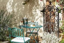 a Provence-inspred outdoor space with a green metal table and chairs, potted plants and blooms and some lanterns