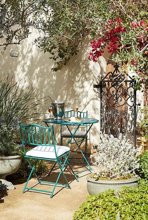 a Provence-inspred outdoor space with a green metal table and chairs, potted plants and blooms and some lanterns