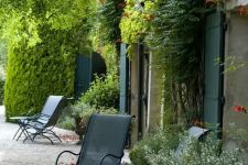 a Provence outdoor space with metal chairs, potted plants and blooms, vines and greenery climbing up the wall of the house