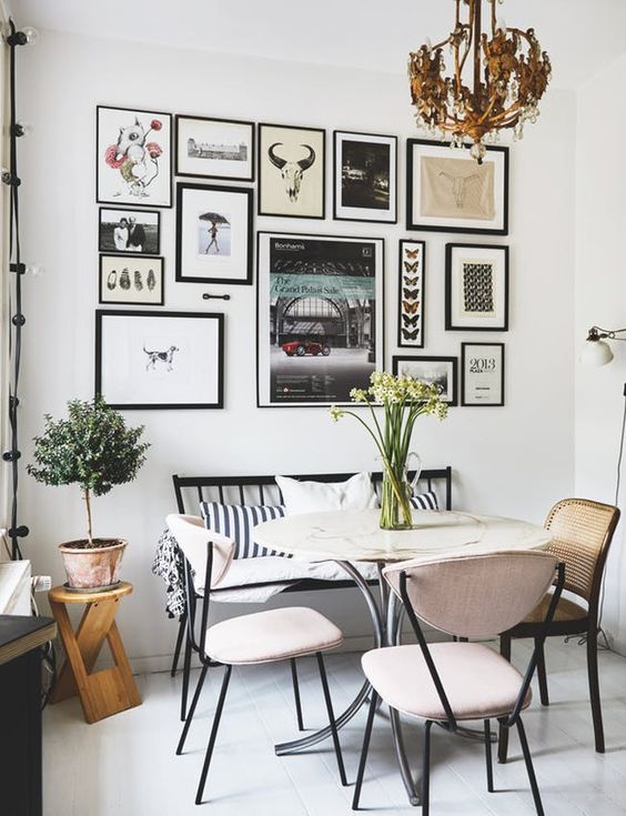 a Scandinavian dining room with a black bench and blush chairs, a stone and metal table, a chic free form gallery wall