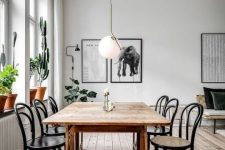 a Scandinavian dining space with a stained table and black chairs, a mini gallery wall, potted plants and a pendant lamp