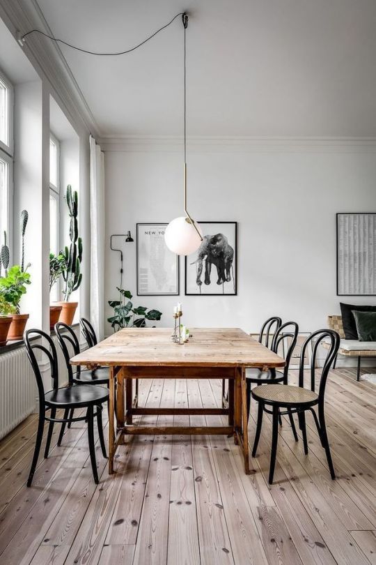 a Scandinavian dining space with a stained table and black chairs, a mini gallery wall, potted plants and a pendant lamp