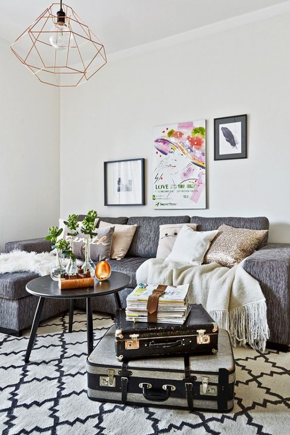 a Scandinavian living room with a grey sectional, a black coffee table, a stack of suitcases and a mini gallery wall