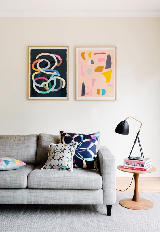 a Scandinavian living room with a grey sofa, a rug, a side table and colorful artwork to add a bit of fun to the space