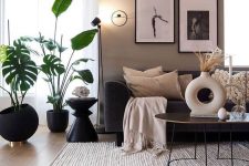 a Scandinavian living room with taupe and greige walls, black furniture, potted plants and a mini black and white gallery wall