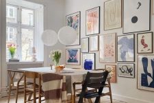 a Scandinavian meets mid-century modern dining room with a simple table and mismatching chairs plus a colorful gallery wall