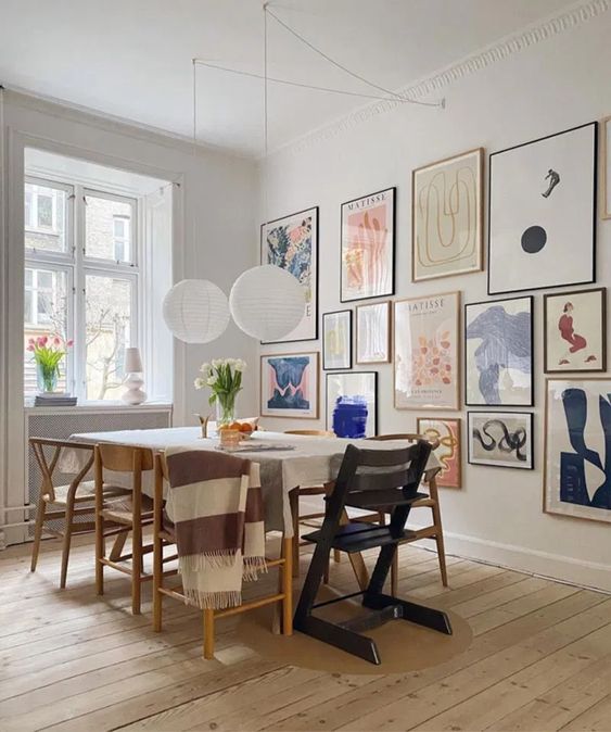 a Scandinavian meets mid century modern dining room with a simple table and mismatching chairs plus a colorful gallery wall