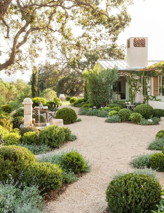 a beautiful Spanish-inspired garden with greenery and gravel pathways, with some trees and vintage furniture