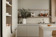 a beautiful and soothing grey kitchen with no hardware cabinets, a large kitchen island, storage units, copper items and wooden stools