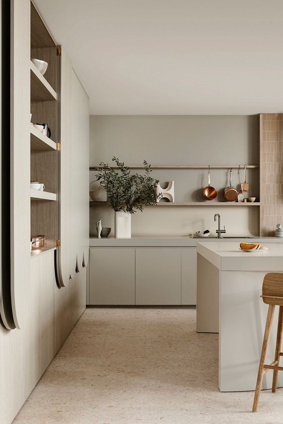 a beautiful and soothing grey kitchen with no hardware cabinets, a large kitchen island, storage units, copper items and wooden stools