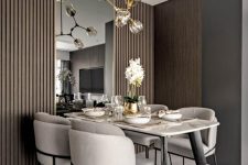 a beautiful contemporary dining space with a marble top table, neutral chairs, a large mirror, taupe wooden panels and a catchy chandelier