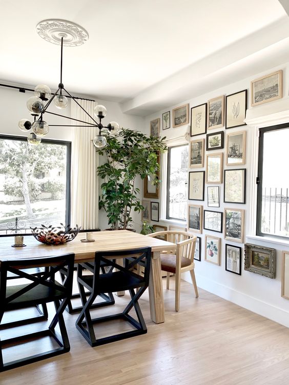 a beautiful dining room with a light stained table and mismatching chairs, a chic chandlier and a monochromatic gallery wall
